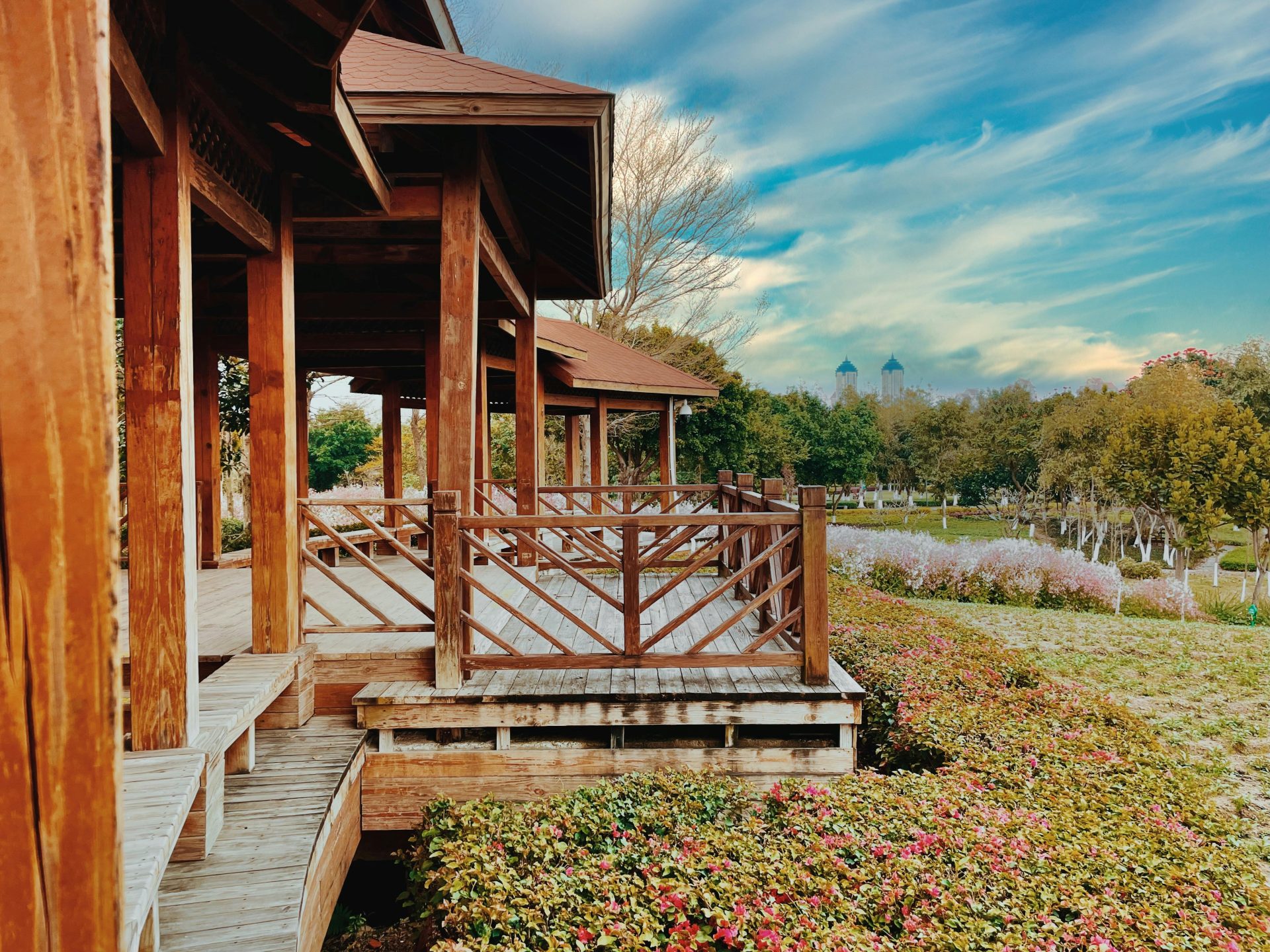 Wooden pavilion with rustic charm in a vibrant park, surrounded by lush greenery and colorful flowers.